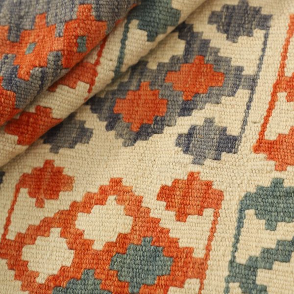 Gefalteter Kelim im Detail, Rauten in Orange und Grau auf Creme